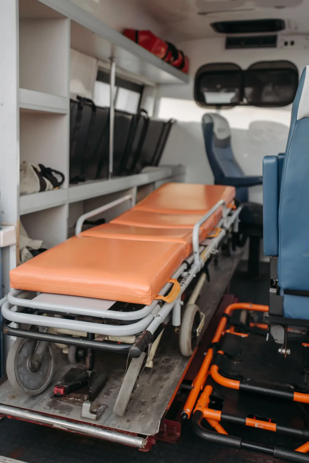 The inside of a patient transport vehicle, with a wheeled stretcher, a wheelchair and seating